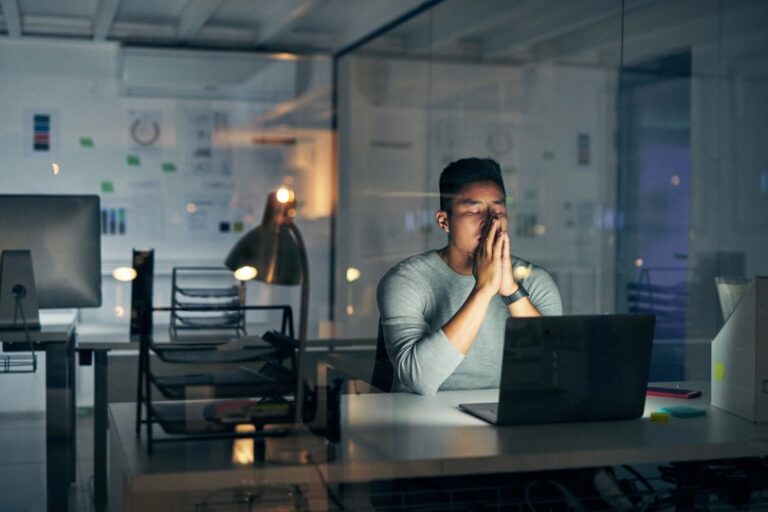 A man working late at a laptop in an office, looking worried