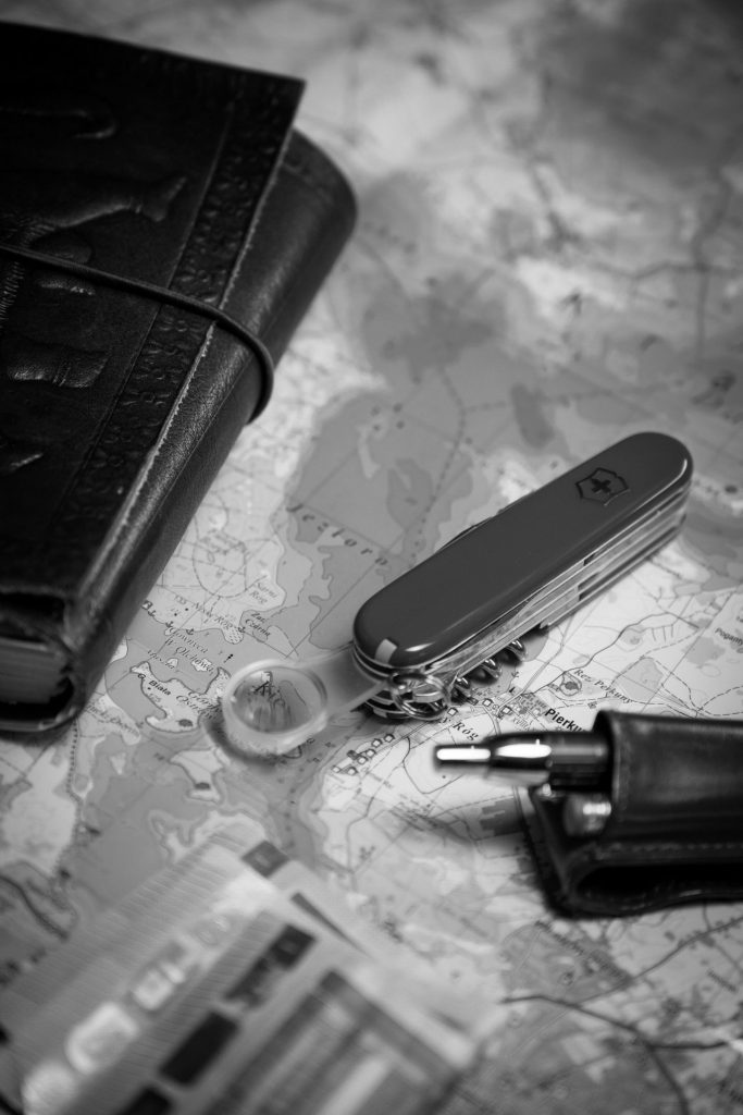 A closed red Swiss army knife on a map beside a leather wallet and a pen