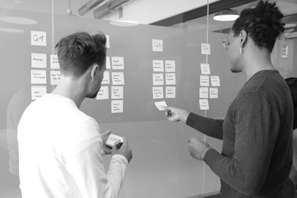 Two people arranging sticky notes on a glass wall