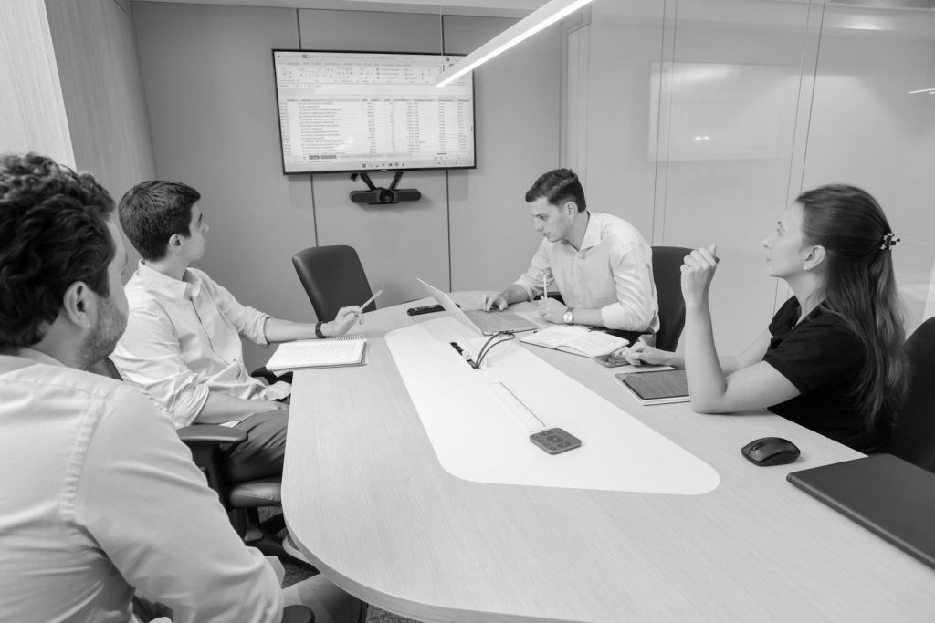 A meeting around a boardroom table with a dashboard on the screen