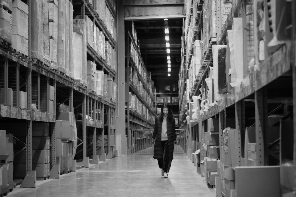 A woman walking down a warehouse aisle between tall shelves