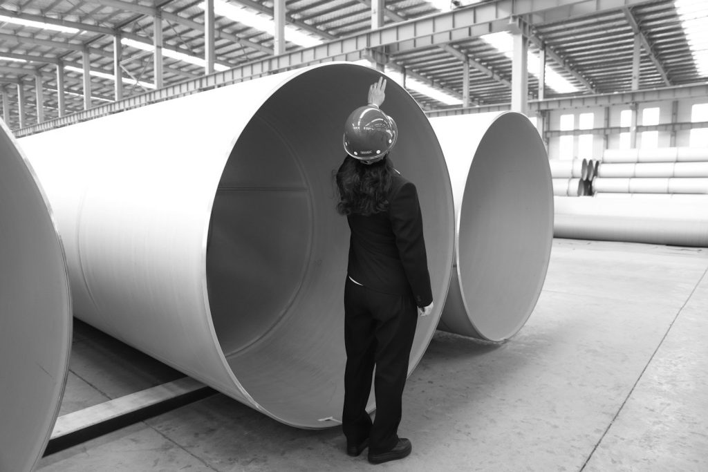 An engineer in a hard hat inspecting large steel pipes in a factory