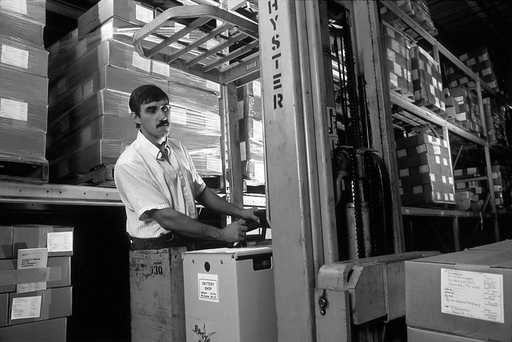 A man driving a forklift among stacked boxes in a warehouse