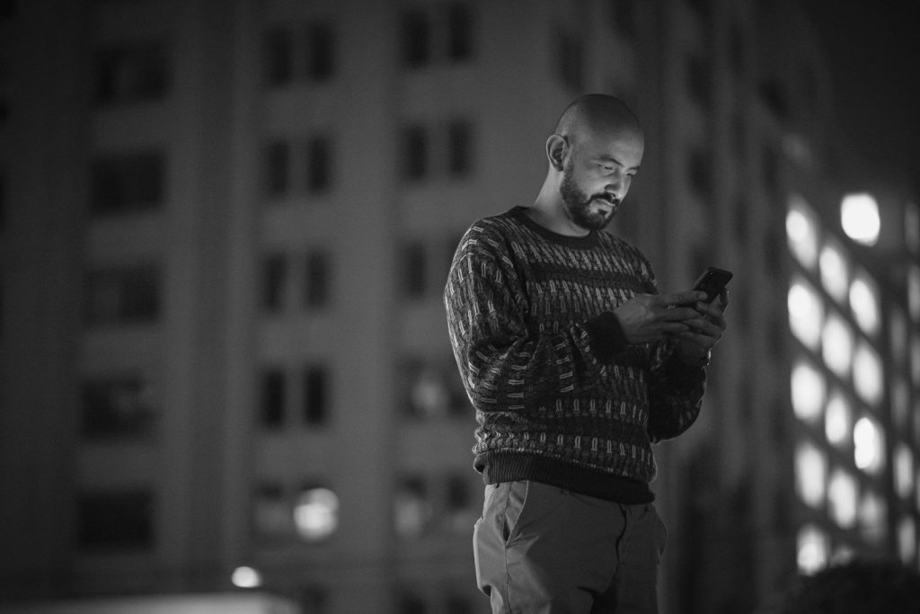 A man checking his phone in front of an office building at night